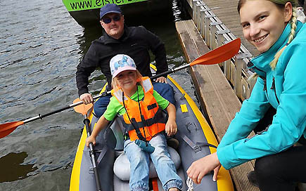 Erzieherschülerin der DPFA Leipzig, Heidi, hilft einem Kita-Vater und seiner Tochter in ein Schlauchpaddelboot im Leipziger Eltersflutbecken.